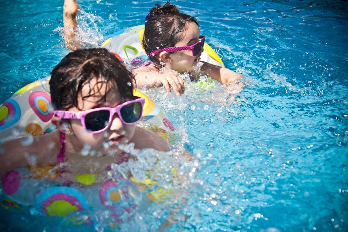 Parent applying sunscreen to a young child's shoulders at a pool