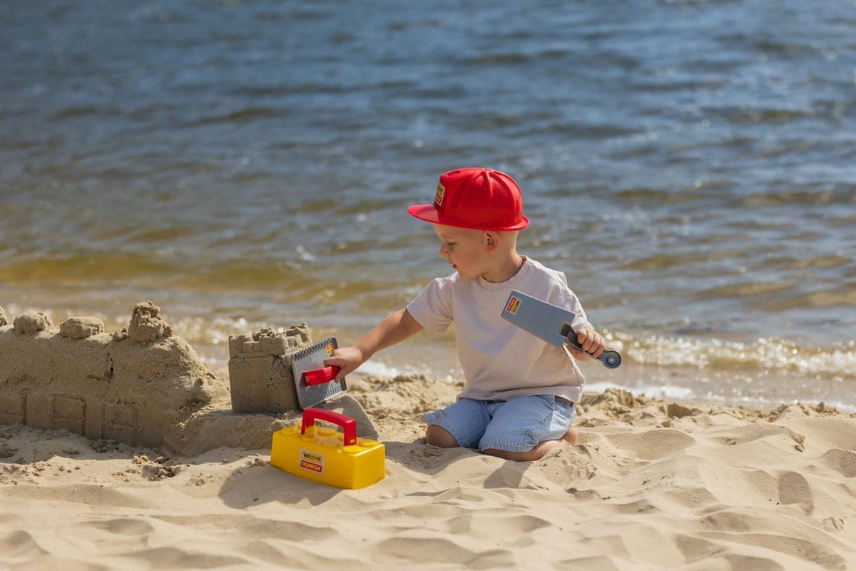 Young child in a wide-brim hat and long-sleeve swim shirt at the water's edge