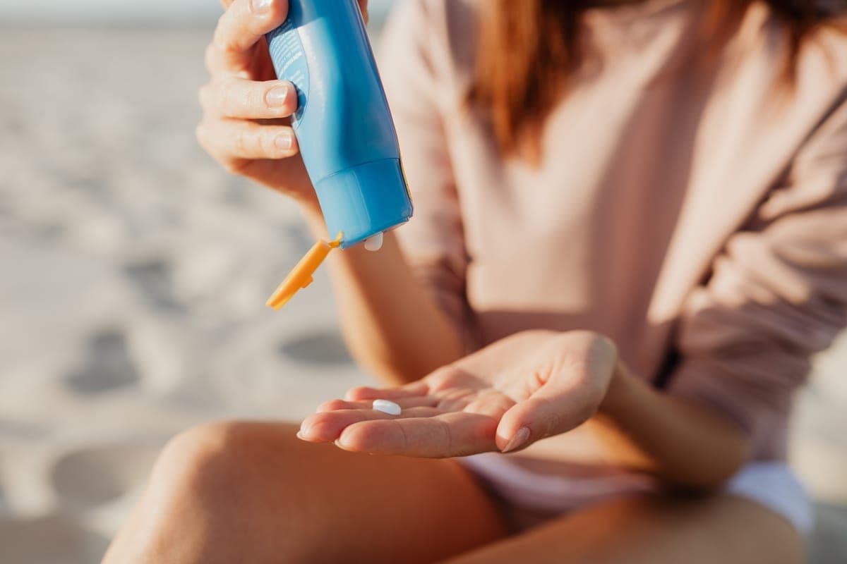 Adult applying sunscreen to a forearm on a bright open beach